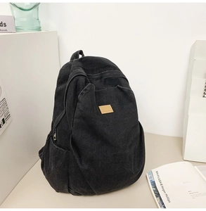 Detail view of washed black denim backpack with leather patch and side pocket storage