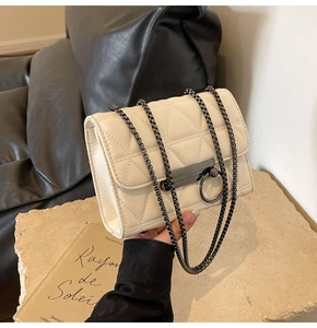 Macro shot of cream quilted crossbody bag with metal ring buckle and square chain detail