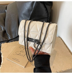 Detail of white quilted chain bag with dark metal ring buckle on stone surface