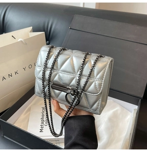 Close-up of silver quilted chain bag with unique metal bar clasp on a luxury gift box