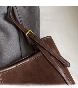 Detail of adjustable long shoulder strap with gold metal buckle on brown suede tote bag