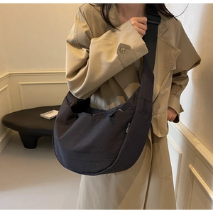 Detail of black nylon half-moon crossbody bag with adjustable strap on beige coat
