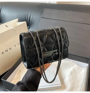 Close-up of black quilted crossbody bag with metal chain strap and luxury gift packaging