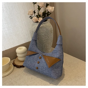 Gros plan du sac sous le bras en denim bleu avec revers en cuir marron et boutons décoratifs