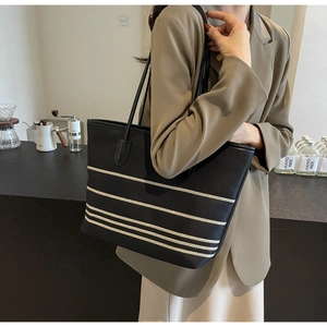Striped canvas tote bag detail showing black leather straps and premium texture finish
