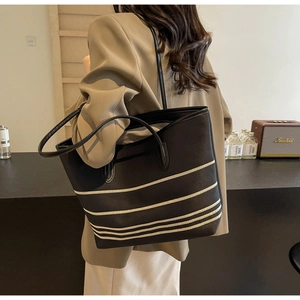 Detailed side view of a large black striped canvas tote bag worn by a model