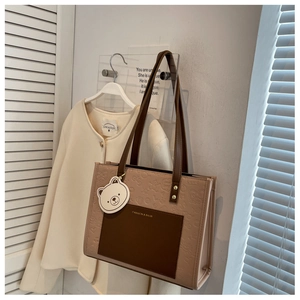Detail der geprägten Tragetasche mit brauner Tasche und süßem Bärenanhänger in Beige