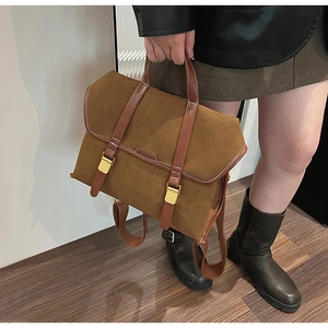 Detail view of brown suede satchel featuring contrast leather straps and gold metal buckles