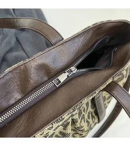 Detail of silver metal zipper and brown leather trim on leopard print tote bag