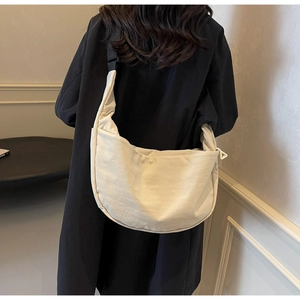 Model wearing a minimalist cream canvas crossbody moon bag with adjustable black strap
