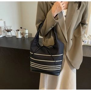 Detail of black canvas tote bag showing striped pattern and delicate leather bow tie
