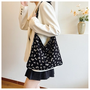 Side view of a large black tote bag with white bow patterns worn by a model in a room