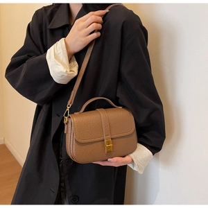 Close-up of brown pebbled leather crossbody bag with golden square twist lock on a model