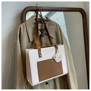 Detail einer geprägten Shopper-Tasche mit braunem Besatz an einem beigen Trenchcoat