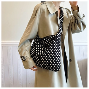 Detail of black polka dot canvas tote bag with EMIS side label on casual trench coat