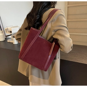 Detailed view of dark burgundy suede tote bag worn over the shoulder in a cozy cafe setting
