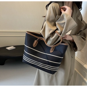 Detail of a large striped canvas tote bag with brown leather handles on a beige coat