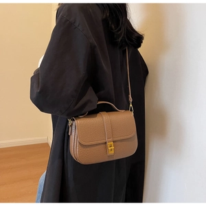 Detail of dark brown leather crossbody bag featuring lychee texture and gold buckle