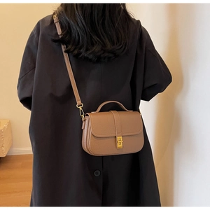 Detail view of a brown pebbled leather crossbody bag on a model wearing a black coat