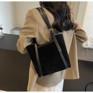 Detail of black suede tote bag with leather trim and gold buckle on a model shoulder