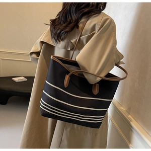 Detail of black striped canvas tote bag with brown leather straps on trench coat model