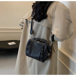 Detailed close-up of a black pleated leather crossbody bag with a wide striped strap