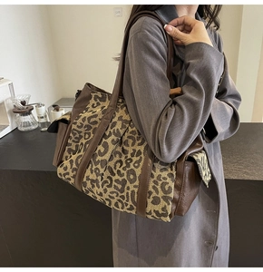 Detail view of large leopard print tote bag with brown leather accents on model
