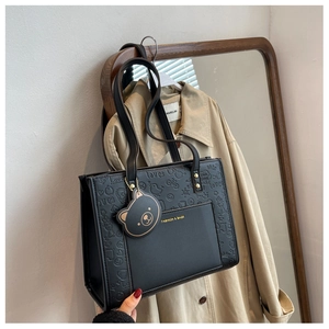 Detail der schwarzen geprägten Shopper-Tasche mit Herzmuster und Bären-Anhänger