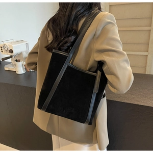 Detail view of the black suede tote bag with leather trim on a shoulder-slung model