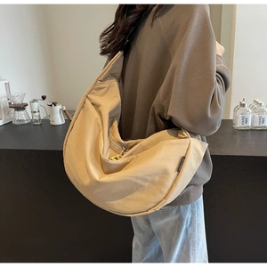 Detail view of large beige crescent crossbody bag with black strap and metallic zipper