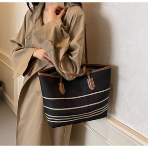 Detail of striped canvas tote bag with brown leather handles worn by a model in a trench coat
