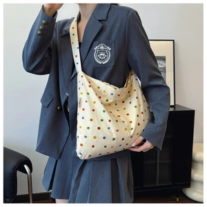 Detail shot of a large beige canvas hobo bag featuring colorful polka dots and wide strap