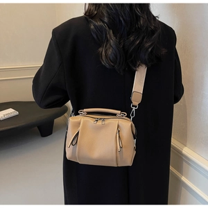 Detailed back view of khaki pebbled leather bag with a wide strap on a black coat