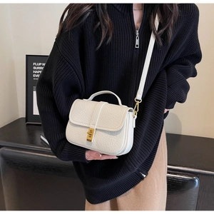 Close-up of beige leather crossbody bag with metallic gold lock and handle detail