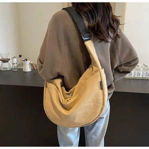 Detail of khaki crescent crossbody bag with wide black strap in a cozy cafe setting