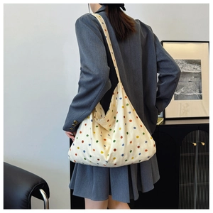 Lifestyle shot showing a cream canvas tote bag with colorful dots worn on the shoulder