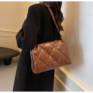 Detail of brown quilted rhombic shoulder bag with adjustable strap on a black coat