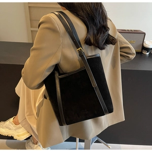 Detail of black suede tote bag featuring leather trim and gold metal buckle on shoulder strap
