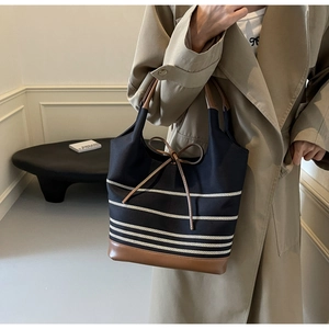 Detail of striped canvas tote bag featuring brown leather trim and bow knot decoration