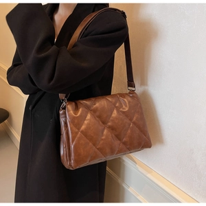 Detail of brown quilted faux leather shoulder bag with wide strap and metallic hardware