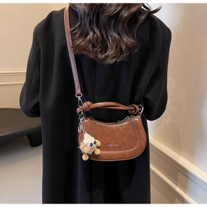 Detailansicht einer braunen Hobo-Tasche mit Plüsch-Anhänger auf einem schwarzen Wollmantel