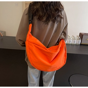 Detail of a bright orange crescent crossbody bag featuring an adjustable wide black strap