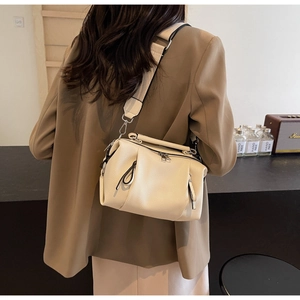 Detail of beige textured leather pillow bag featuring a wide fabric shoulder strap