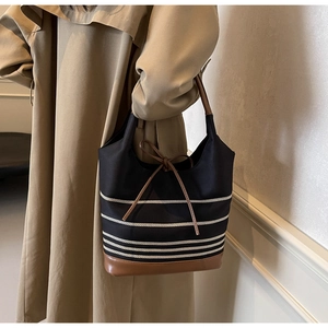 Detail of striped canvas tote with brown leather handles worn with a beige trench coat
