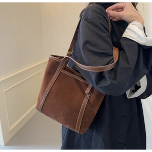 Brown suede tote bag with leather straps shown from a side view on a female model