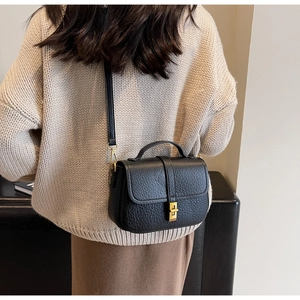 Crossbody wear display of a black lychee texture leather handbag with gold metal clasp