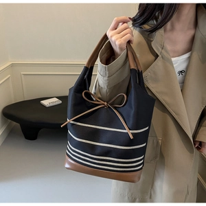 Detail of the canvas tote bag showing the brown leather handle and white striped accents