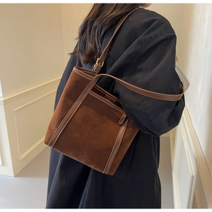 Detail view of brown suede tote bag with leather straps and large front pocket on a model