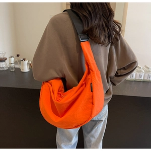Bright orange nylon crescent bag shown worn by a model in a modern cafe setting