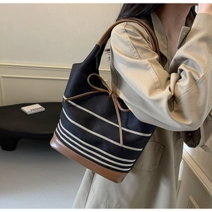 Detailed side view of canvas bucket bag featuring stripes and brown leather trim